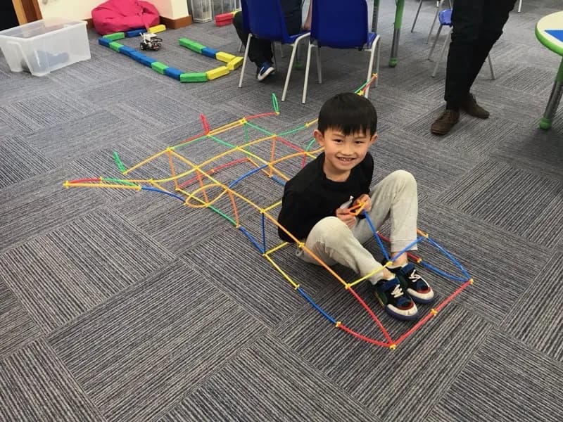 A child sitting inside a large frame built from construction straws